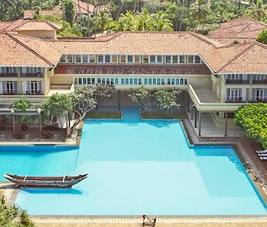 Ein weitläufiger Pool umgeben von tropischen Pflanzen und einem eleganten Gebäude mit traditioneller Architektur.