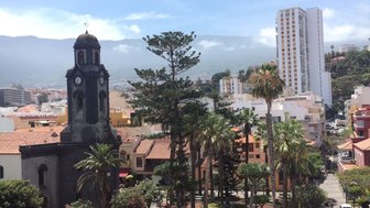 Ein Blick auf den lebhaften Platz in Puerto de la Cruz, umgeben von Palmen und bunten Gebäuden unter einem blauen Himmel.