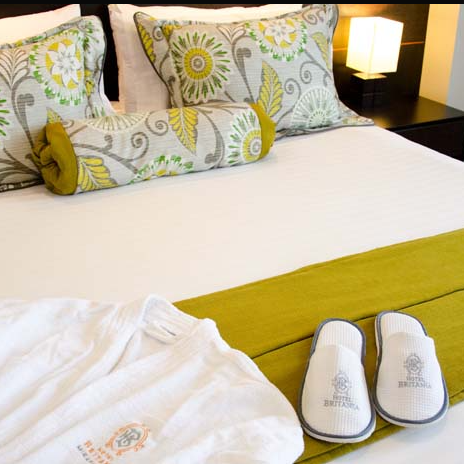 Ein einladendes Hotelzimmer mit einem komfortablen Bett, dekorativen Kissen und einem weichen Bademantel auf der Bettdecke.
