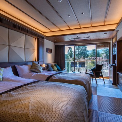 Ein stilvolles Hotelzimmer mit zwei Betten, eleganten Kissen und einem großen Fenster, das auf eine grüne Landschaft blickt.