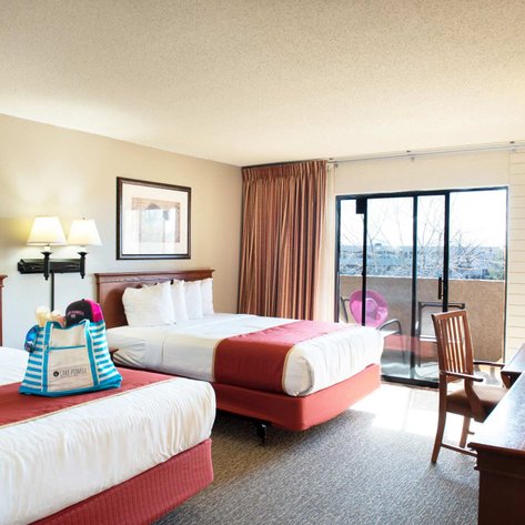 Ein helles Hotelzimmer mit zwei Betten, einem Schreibtisch und einem Balkon, der einen Blick auf die Umgebung bietet.