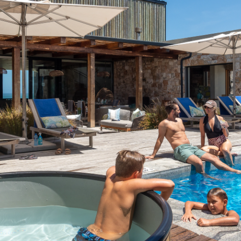 Eine entspannte Familie genießt einen sonnigen Tag am Pool des Morukuru Beach Lodge mit Liegen und Sonnenschirmen.