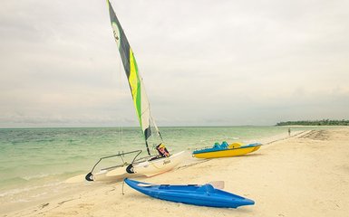 Ein Katamaran mit buntem Segel liegt am Strand, während ein Kajak und ein weiteres Boot in der Nähe warten.