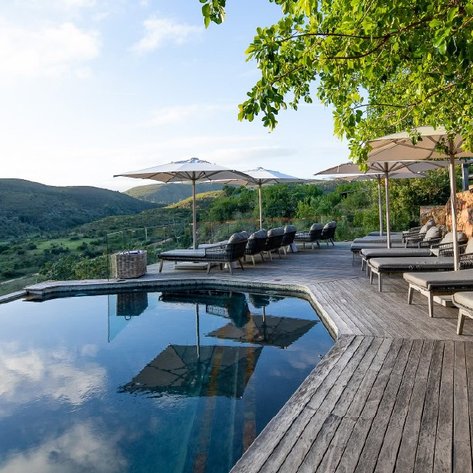 Ein ruhiger Poolbereich mit Liegen und Sonnenschirmen, umgeben von sanften Hügeln und üppiger Vegetation.