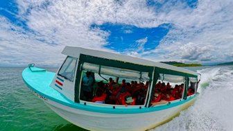 Ein schnell fahrendes Boot mit Passagieren schneidet durch das grüne Wasser, während die Wolken am Himmel dramatisch wirken.