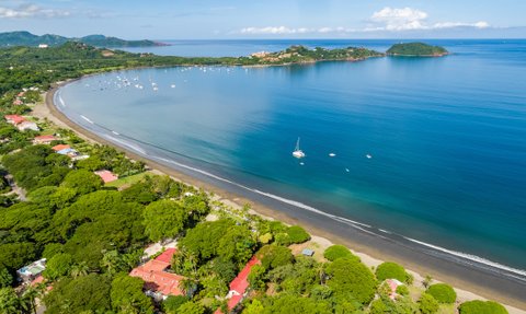 Eine atemberaubende Küstenansicht mit sanften Wellen, Booten im Wasser und üppigem Grün entlang des Strandes.