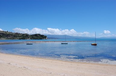 Ein ruhiger Strand mit feinem Sand, sanften Wellen und mehreren Booten, die im klaren Wasser schwimmen.