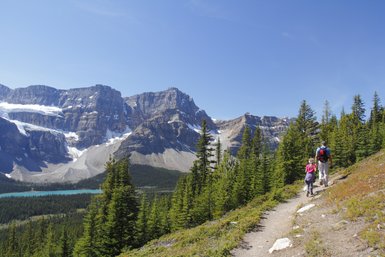 Ein Wanderer und ein Kind erkunden einen malerischen Pfad in den Rocky Mountains, umgeben von majestätischen Bergen und Nadelbäumen.