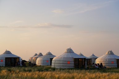 In der sanften Abenddämmerung stehen mehrere Jurten in einer weiten Graslandschaft, umgeben von sanften Hügeln.