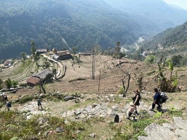 Eine Gruppe von Wanderern geht einen steinigen Pfad hinunter, umgeben von terrassierten Feldern und Bergen in Nepal.