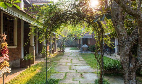 Ein malerischer Gartenweg, gesäumt von Bäumen und Pflanzen, führt zu einem charmanten Gebäude im Hintergrund.