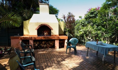 Eine einladende Terrasse mit einem offenen Kamin, umgeben von üppigem Grün und einem blauen Himmel im Hintergrund.