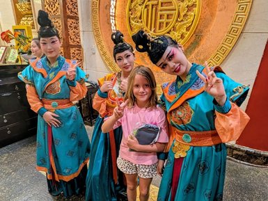 Eine Gruppe von vier Frauen in traditionellen Kostümen posiert begeistert mit einem Mädchen in der Mitte, das den Frieden zeigt.