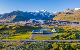 Eine weitläufige Landschaft mit einem Hotel im Vordergrund, umgeben von grünen Wiesen und majestätischen Bergen im Hintergrund.