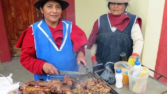 Zwei Frauen in traditioneller Kleidung stehen an einem Grill, während sie köstliches gegrilltes Fleisch zubereiten.