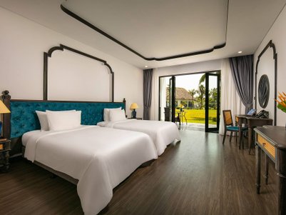 Ein elegantes Zimmer mit zwei Einzelbetten, blauen Akzenten und Blick auf einen grünen Garten durch große Fenster.