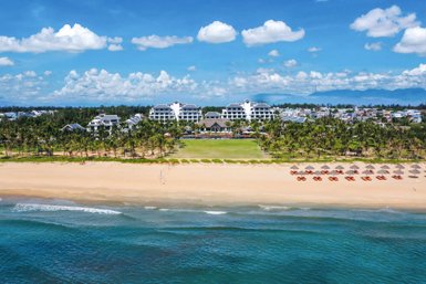 Ein atemberaubender Blick auf den Hoi An Strand mit einem luxuriösen Resort im Hintergrund und Palmen, die sanft im Wind wiegen.