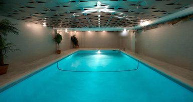 Ein eleganter Innenpool mit leuchtend blauem Wasser, umgeben von modernen Wänden und sanften Pflanzen in Töpfen.