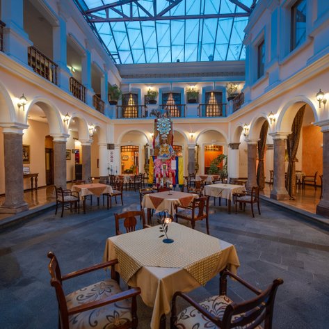 Ein eleganter Restaurantbereich mit Tischen und Stühlen, umgeben von Säulen und einer gläsernen Decke, die Tageslicht hereinlässt.