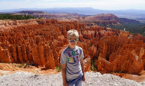 Ein Junge mit Sonnenbrille steht vor den beeindruckenden, orangefarbenen Felsformationen des Bryce Canyon Nationalparks.