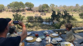Familie mit Kindern genießt ein Frühstück am Wasserloch und beobachtet dabei Elefanten – Südafrika Familienreise