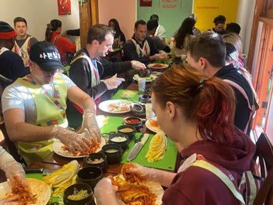 Eine Gruppe von Menschen bereitet Kimchi in einer Kochschule vor, während sie konzentriert an einem Tisch arbeiten.