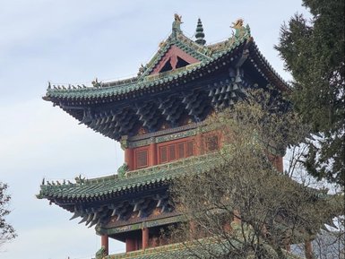 Ein majestätischer Pagodenturm mit kunstvollen Dachdetails erhebt sich über traditionelle, rote Gebäude im Vordergrund.