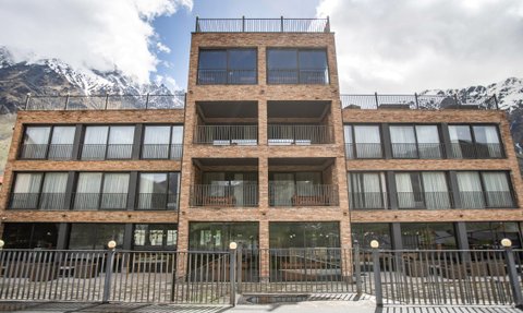 Ein modernes Hotelgebäude aus Ziegelstein mit großen Fenstern und Balkonen, umgeben von majestätischen Bergen.