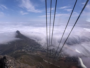 Ein Blick auf die Wolken, die einen Berg umhüllen, während Seile einer Gondelbahn im Vordergrund sichtbar sind.
