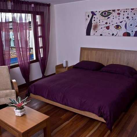 Ein gemütliches Zimmer mit einem großen Bett in lila Bettwäsche und einem Holzrahmen, umgeben von warmen Holzböden.