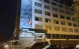 Das Hotel Britania in Miraflores, Peru, erstrahlt nachts mit einer beleuchteten Fassade und einer peruanischen Flagge.