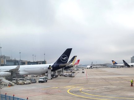 Am Flughafen stehen mehrere Flugzeuge, während ein Mitarbeiter mit Warnweste auf dem Rollfeld arbeitet.