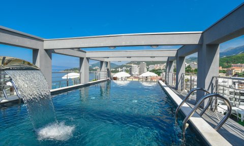 Ein atemberaubender Infinity-Pool mit Wasserfall, umgeben von einer modernen Architektur und Blick auf die Küste von Budva.