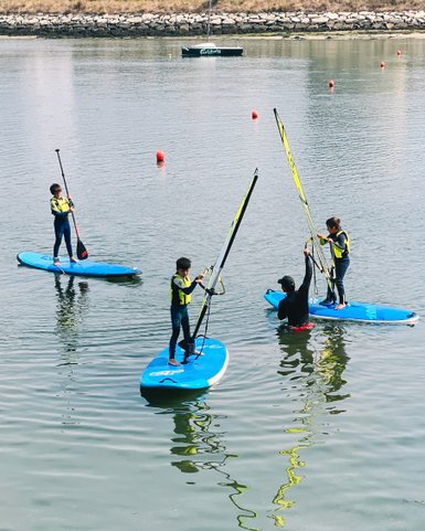 Vier Kinder stehen auf Stand-Up-Paddle-Boards und üben das Paddeln auf einem ruhigen Gewässer in Portugal.