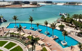 Ein luxuriöser Poolbereich mit Palmen und Liegen, umgeben von klarem Wasser und einem schönen Ausblick auf die Küste.