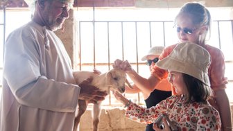 Kinder begegnen einer Ziege bei einem Zwischenstopp auf einer Farm zwischen Canyon und Wüste – Oman Familienreise