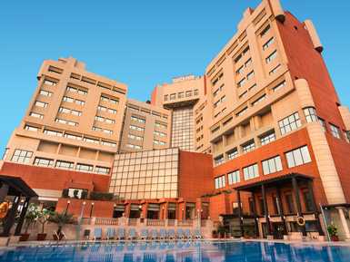 Ein modernes Hotelgebäude mit einer auffälligen Fassade aus roten und beigen Steinen, umgeben von einem klaren blauen Himmel.
