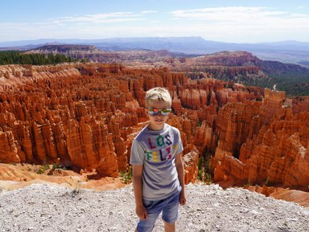 Ein Junge mit Sonnenbrille steht vor den beeindruckenden, orangefarbenen Felsformationen des Bryce Canyon Nationalparks.