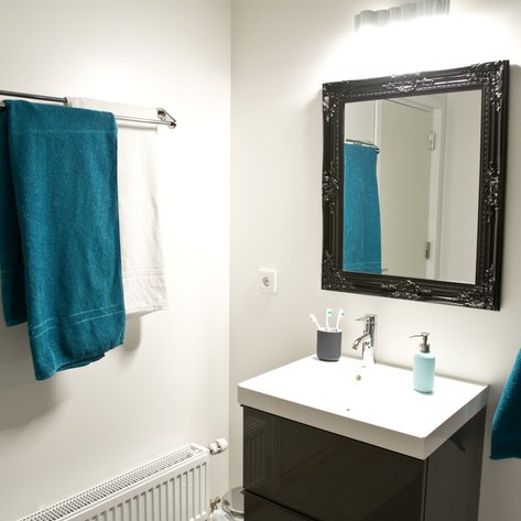 Ein modernes Badezimmer mit einem eleganten Spiegel und Handtüchern in Türkis und Weiß, die an einem Handtuchhalter hängen.