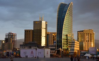 Moderne Wolkenkratzer und ein unvollendetes Gebäude prägen die Skyline von Ulaanbaatar unter einem bewölkten Himmel.