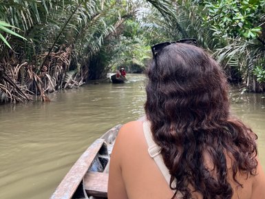 Eine Person mit lockigem Haar sitzt in einem Boot und genießt die ruhige Fahrt durch einen grünen Wasserweg im Mekong-Delta.