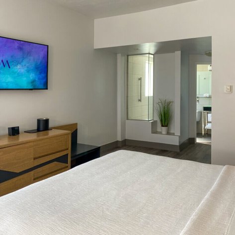 Ein modernes Hotelzimmer mit einem großen Bett, einem Fernseher und einem Badezimmer im Hintergrund ist zu sehen, das viel Tageslicht bietet.