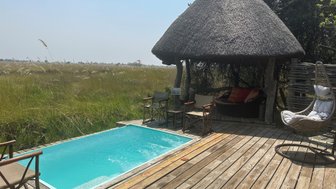 Ein einladender Pool in einem Camp, umgeben von üppigem Gras und einem schattigen Pavillon mit gemütlichen Sitzgelegenheiten.