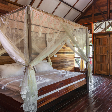 Ein elegantes Bett mit einem Moskitonetz aus zarten Stoffen befindet sich in einem gemütlichen Holzhaus.