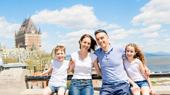 Eine glückliche Familie posiert vor dem beeindruckenden Château Frontenac, umgeben von strahlend blauem Himmel und Wolken.