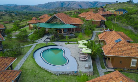 Eine Luftaufnahme des Kigarama Lodges zeigt ein Schwimmbad in Herzform, umgeben von grünen Wiesen und rustikalen Hütten.