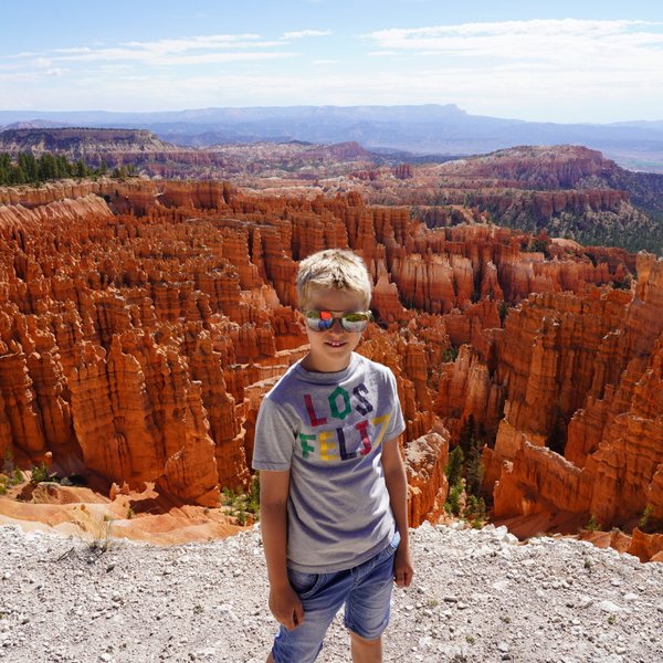 Ein Junge mit Sonnenbrille steht vor den beeindruckenden, orangefarbenen Felsformationen des Bryce Canyon Nationalparks.