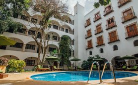 Ein einladender Innenhof mit einem blauen Pool, umgeben von üppigem Grün und gemütlichen Liegen unter Sonnenschirmen.