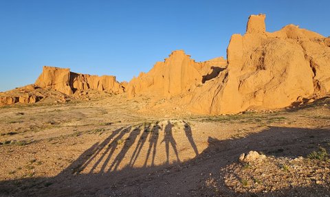 Lange Schatten von Menschen fallen auf die sandige Landschaft der Flaming Cliffs, umgeben von beeindruckenden Felsformationen.