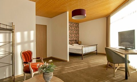 Ein stilvolles Hotelzimmer mit einem großen Fenster, das warmes Licht auf den Boden wirft und eine gemütliche Atmosphäre schafft.